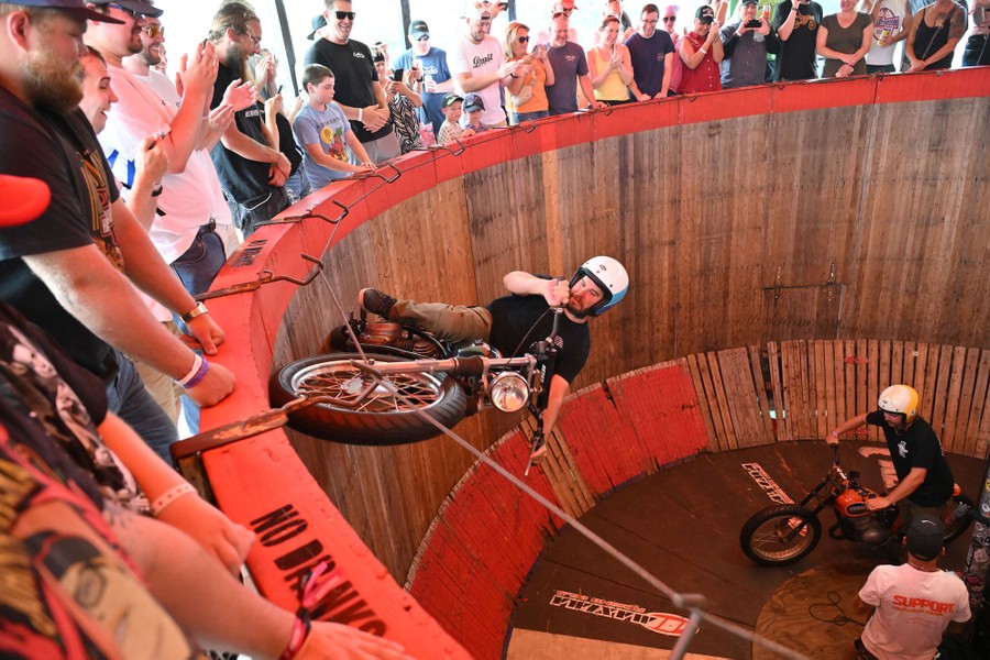 A person rides a motorcycle on a wall inside a round structure, as a crowd above watches.