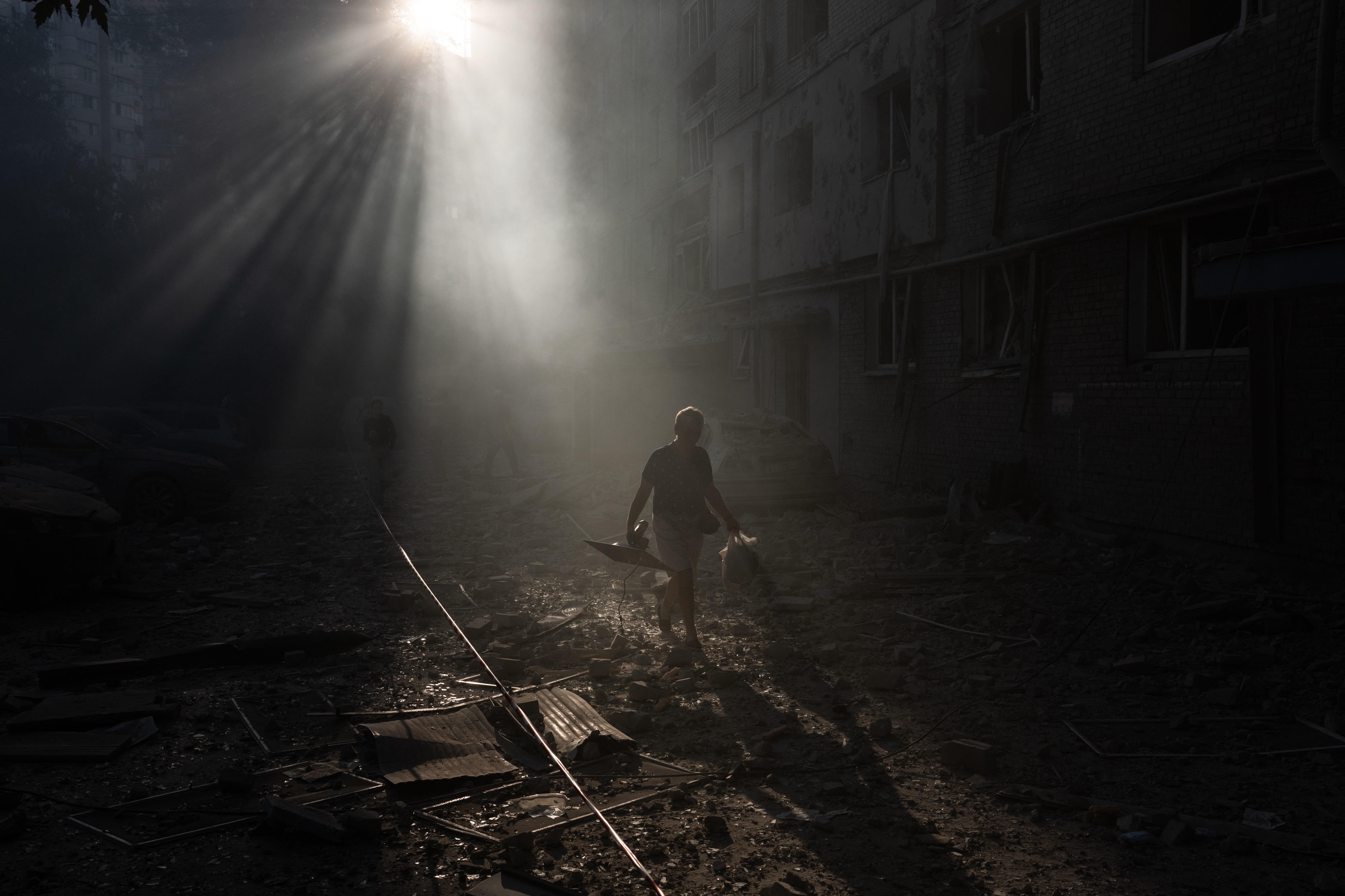 A person walks next a damaged residential building, beneath rays of sunshine visible in dusty air.