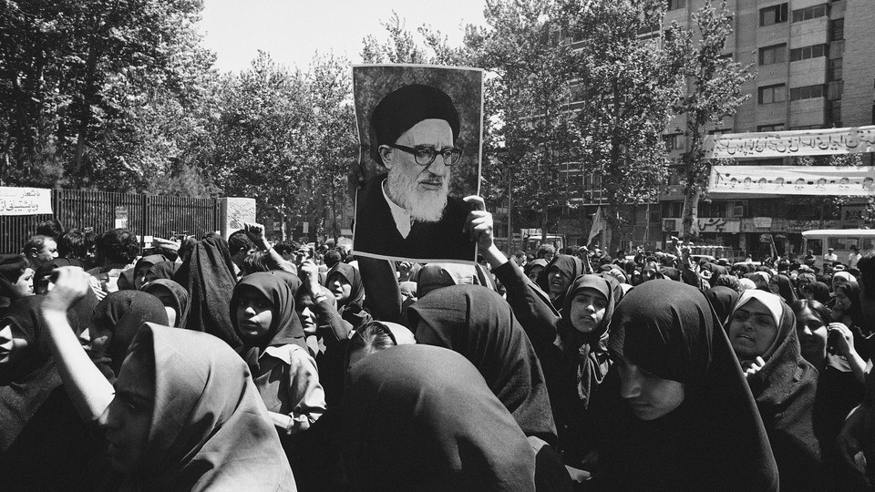 Iranian women wearing chadors hold up a painting of Ayatollah Taleghani. 