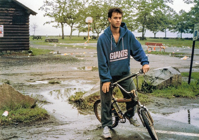 still from movie showing Hanks in Giants hoodie and sweatpants on child's bike in muddy park