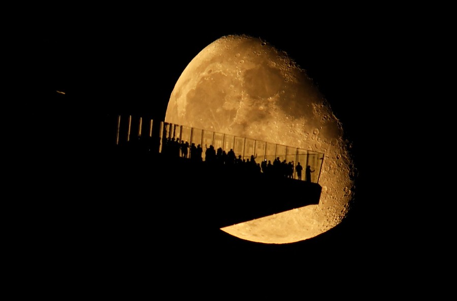 A crowd on a cantilevered observation deck is silhouetted by a rising moon.