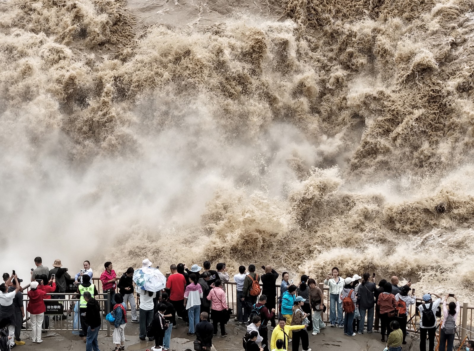 A crowd watches from an observation area as turbulent water, splashes, and rushes past.