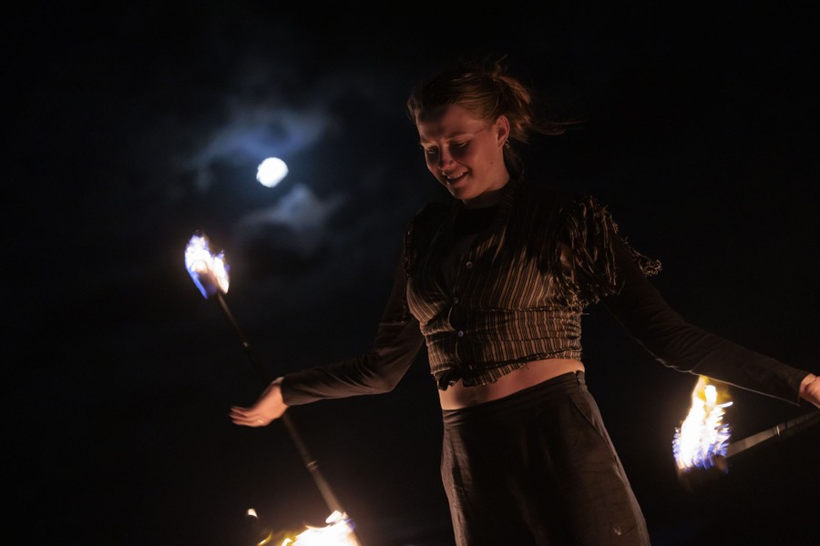 A person twirls two batons with burning ends beneath a moonlit sky.
