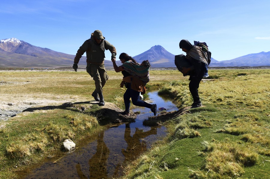 Several people cross a small watery ditch.