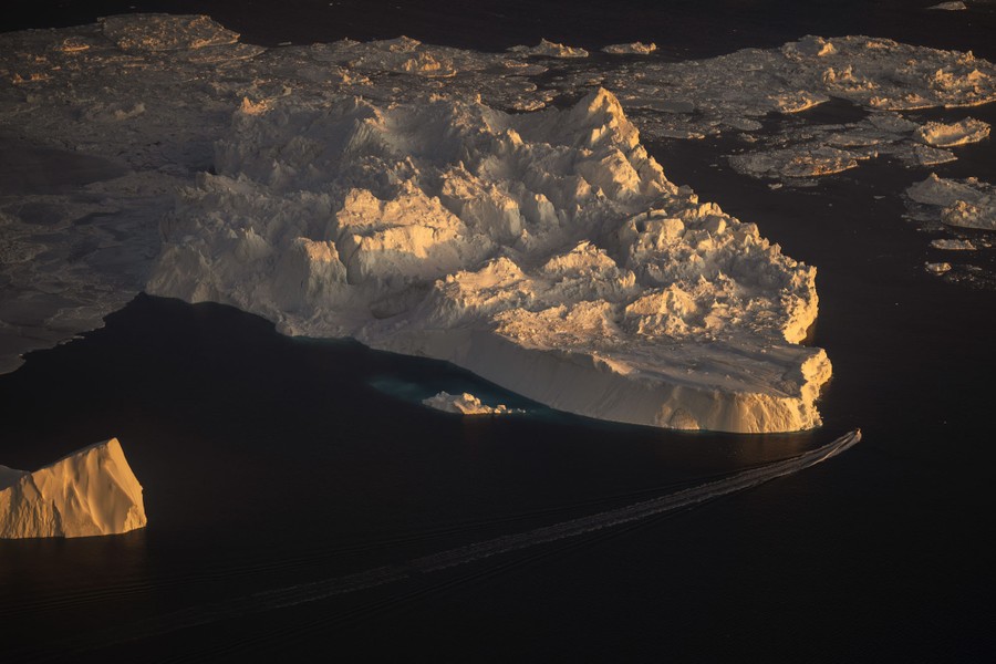 An aerial view of a ship sailing alongside a large iceberg