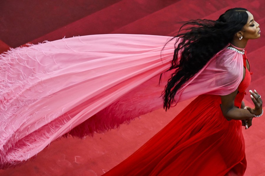 An actress wears a flowing red gown and pink cape.