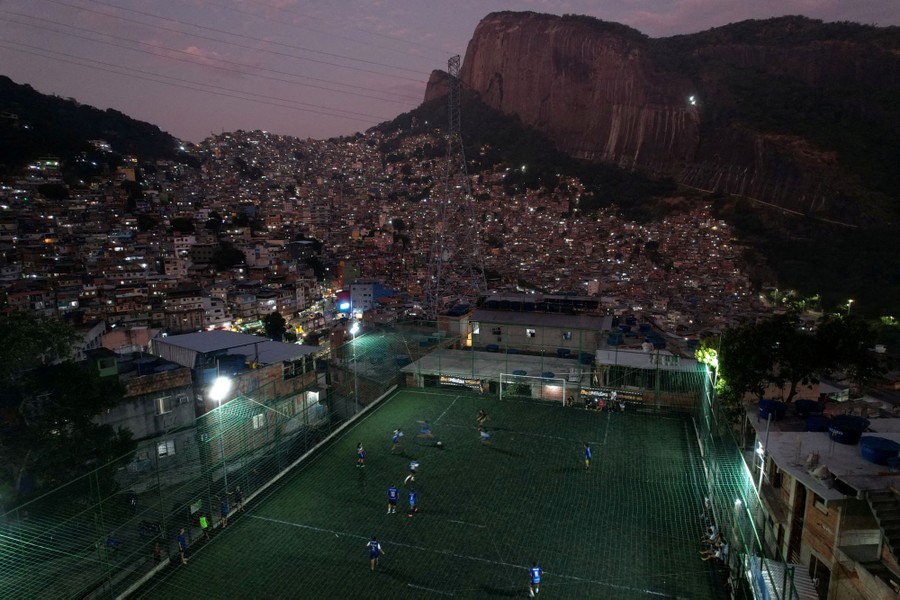 An elevated view of an evening soccer match on a pitch near a hillside favela