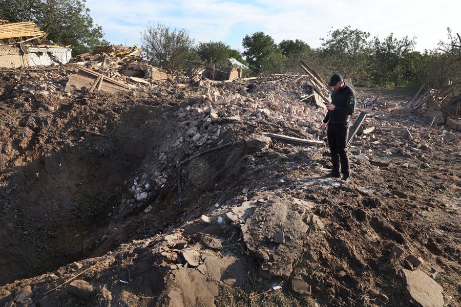 A police officer looks over a large crater left by a missile strike.