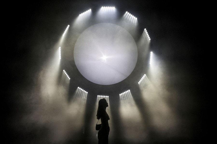 A person stands in front a circular art installation made up of lights and smoke.