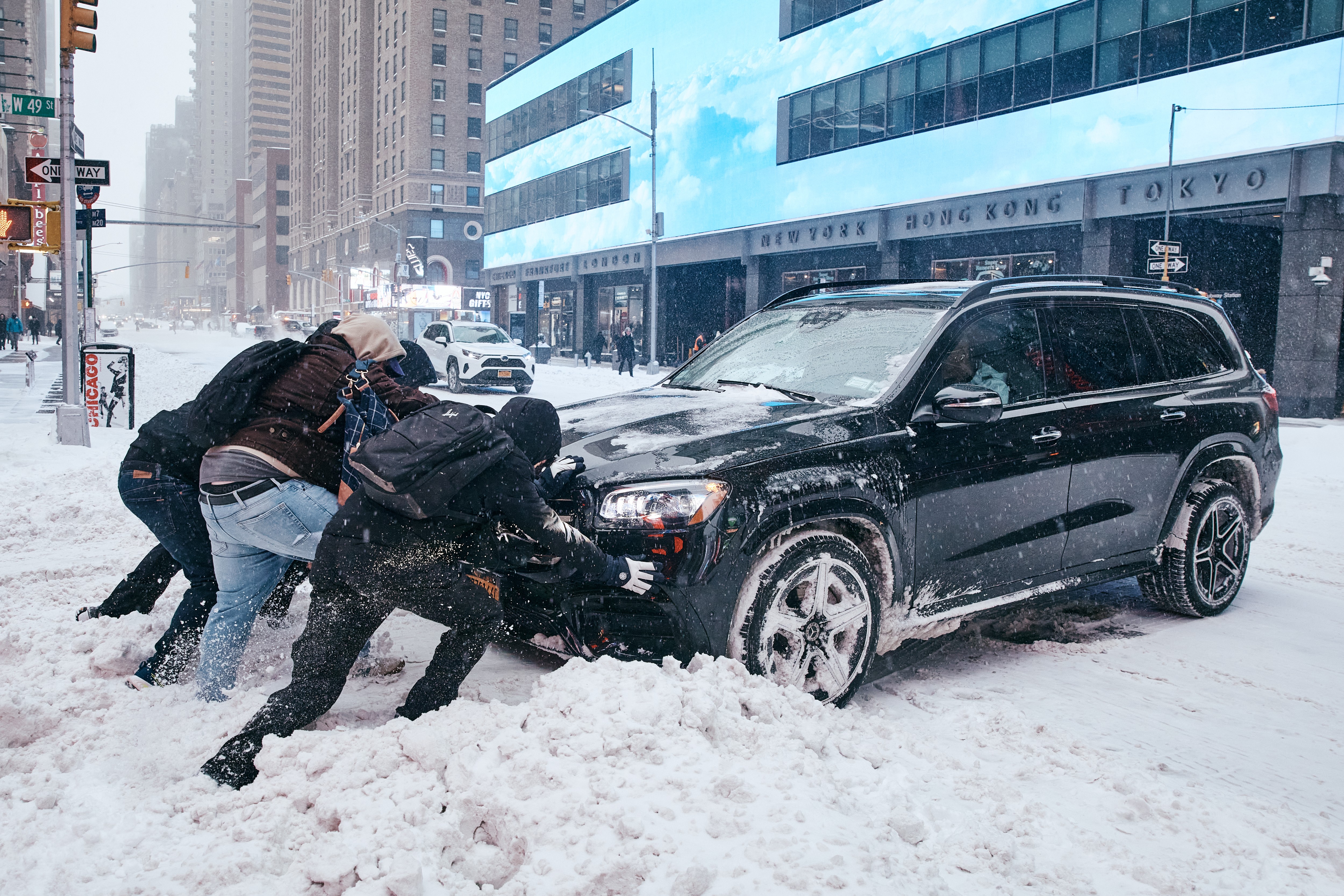 A group of men help to push a car stuck in the snow in a city street.
