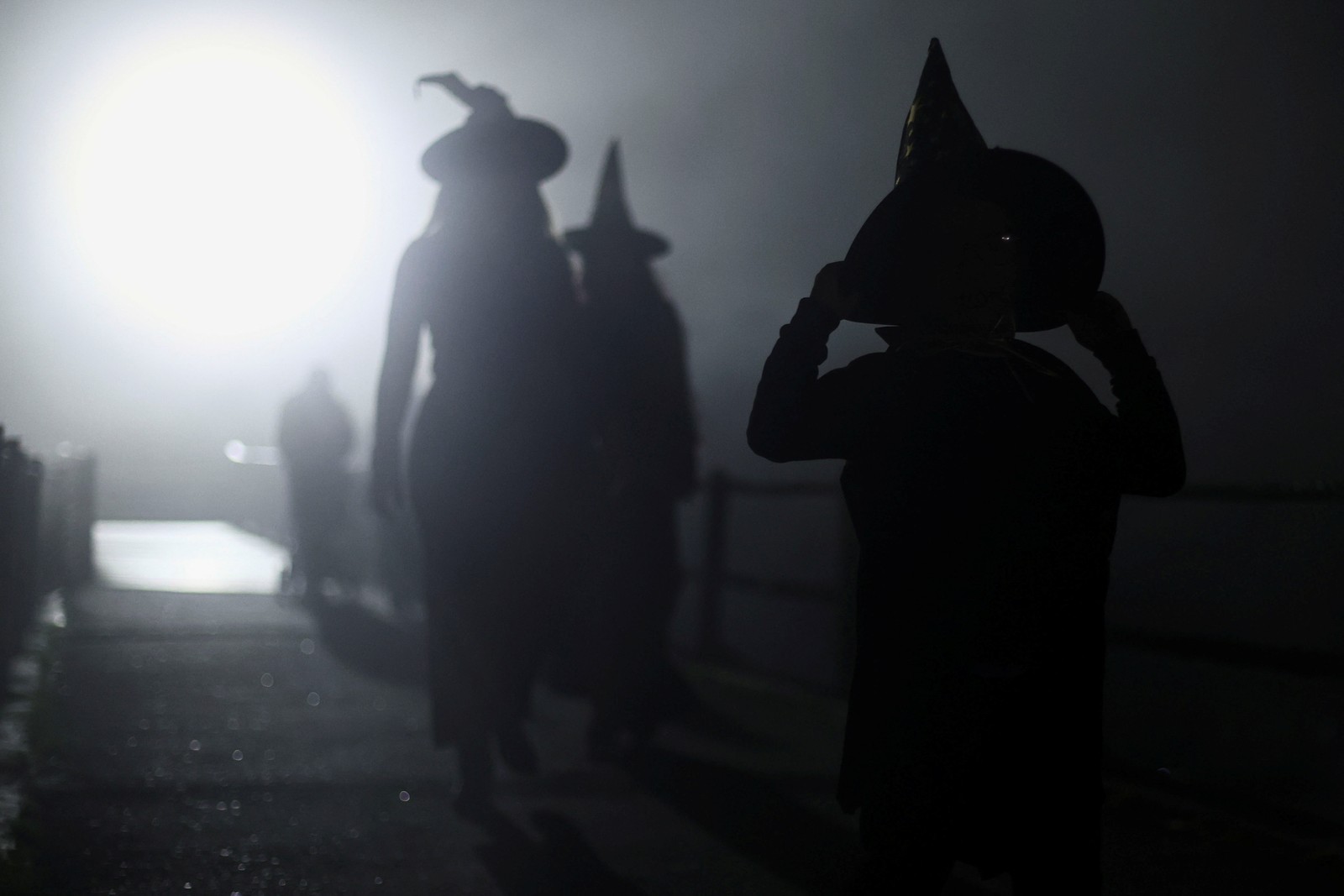 Several people wearing witch costumes walk in a street at night.