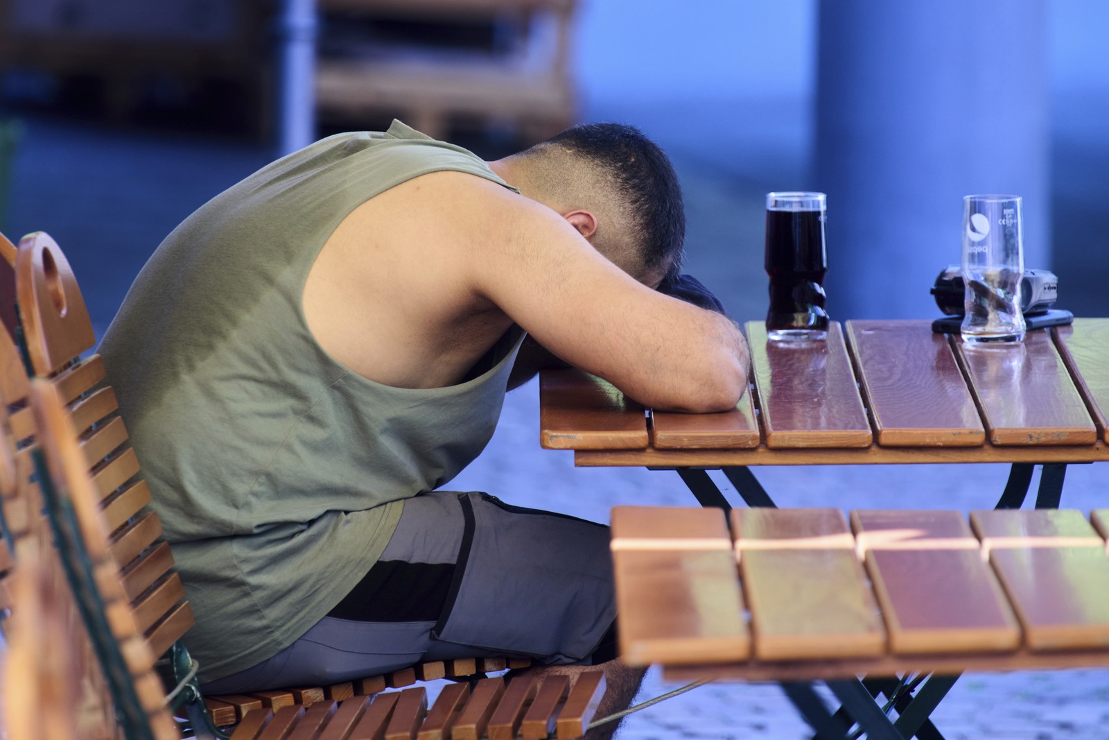 A person rests at a cafe table, their shirt soaked in sweat.