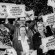 Black-and-white photo of a group of people, most of them holding up signs that say "Make America Wealthy Again"