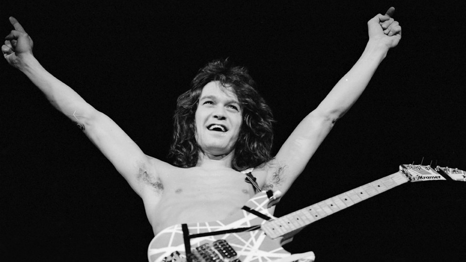 Eddie Van Halen with arms raised while wearing a guitar