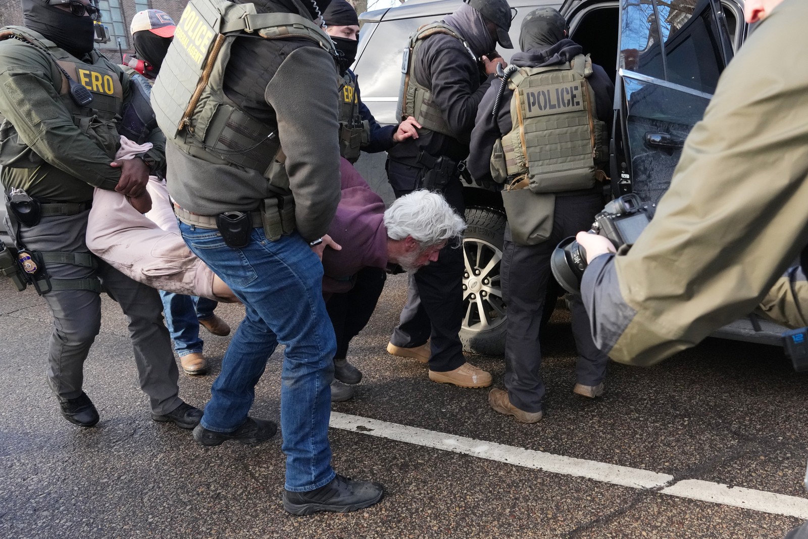 A person who is handcuffed is carried by several federal agents into a car.