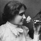 A black and white photograph of Helen Keller smelling a rose