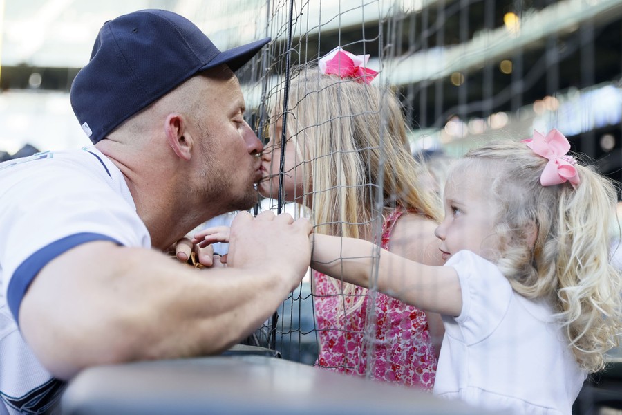 A father kisses his young daughter through a net before a baseball game.