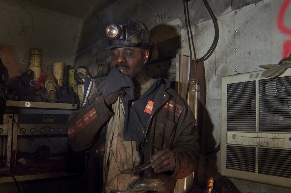 A man wiping coal dust from his face in a dingy work room.
