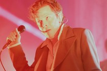 Mike Hadreas, a.k.a. Perfume Genius, onstage with a mic in his hand, bathed in red-pink light