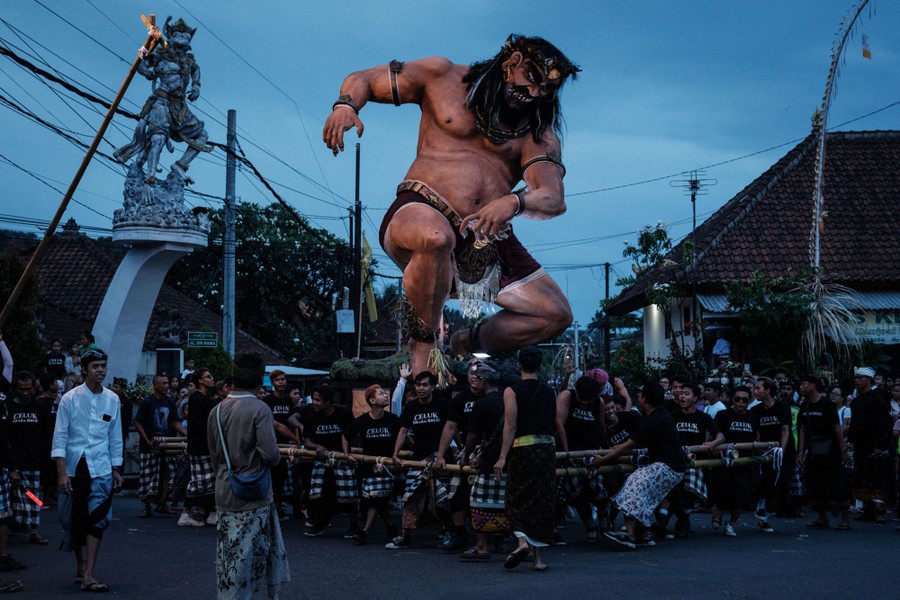 A group of people carry a large statue of a crouching demon before a parade.