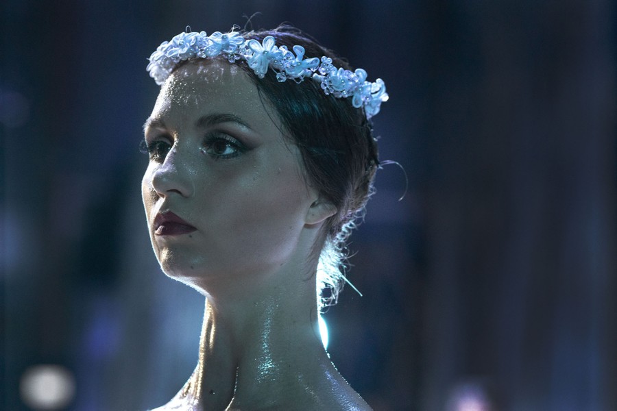 A ballet dancer is onstage, wearing flowers in her hair.