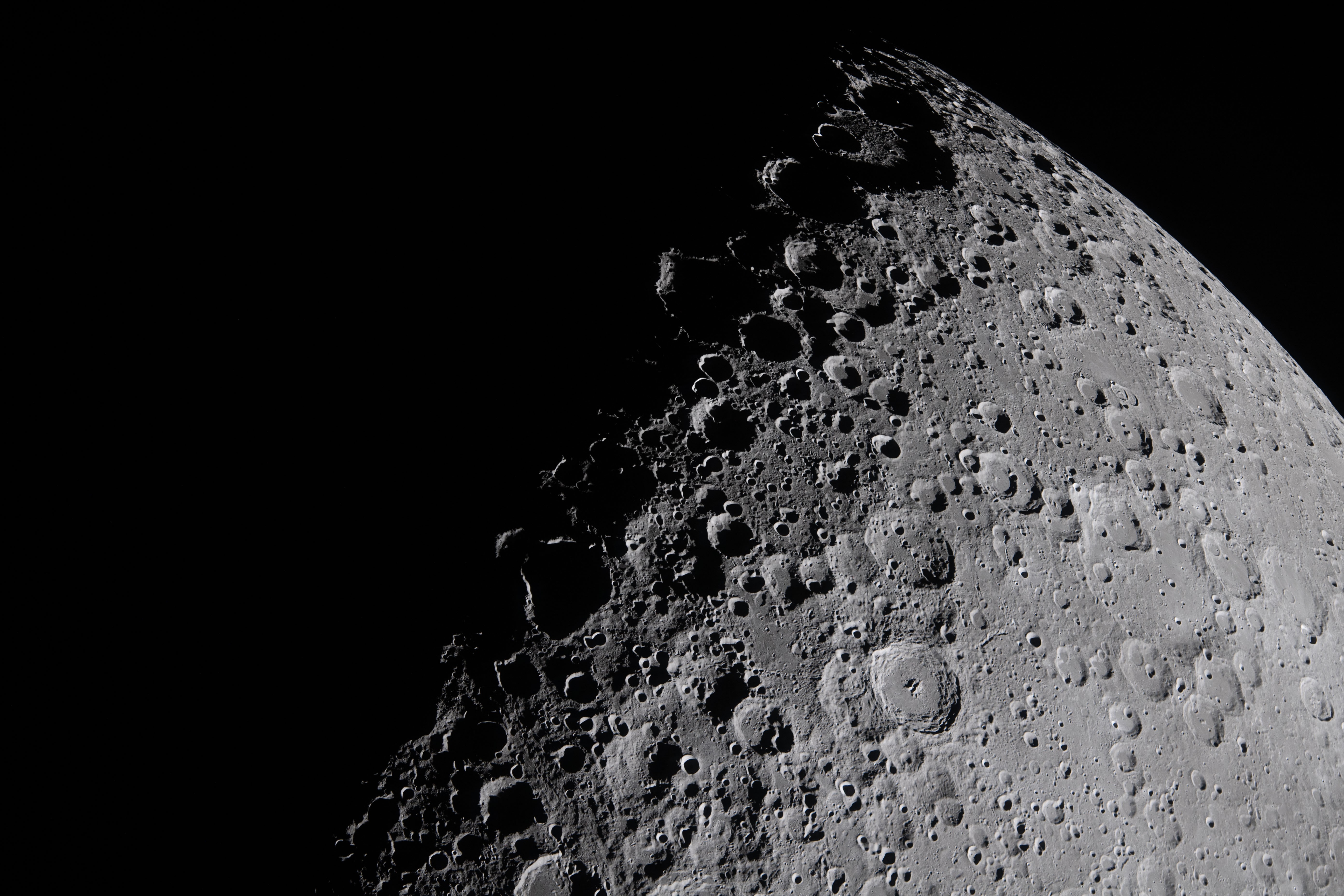 A close view of the surface of the moon, with many visible rugged craters along the line between shadow and sunlight