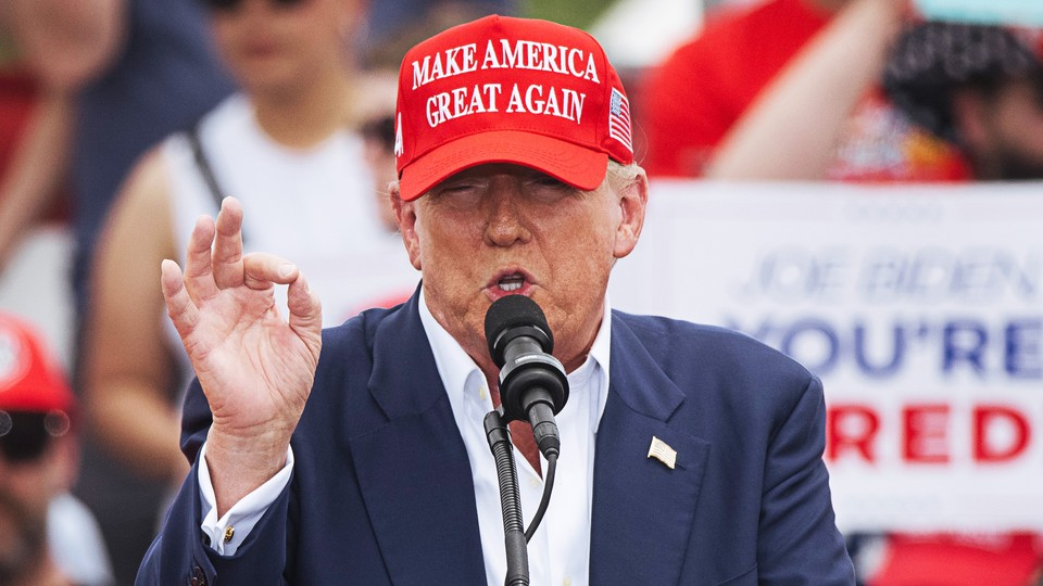 Wearing a red MAGA hat and a blue suit with a flag lapel pin, Trump speaks into a microphone at his recent rally in Las Vegas.