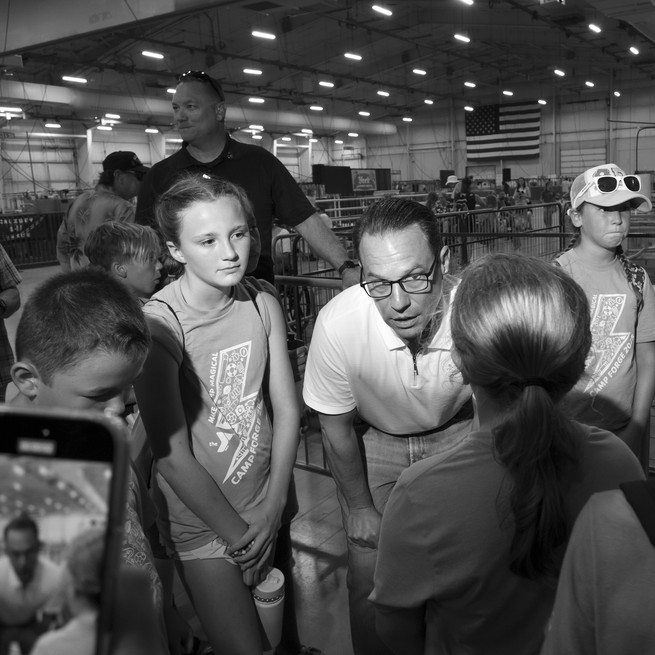 A black and white photograph of Josh Shapiro speaking to a group of young people at a day camp