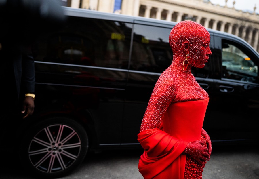 A woman wears a red garment and is completely covered in thousands of small red crystals.
