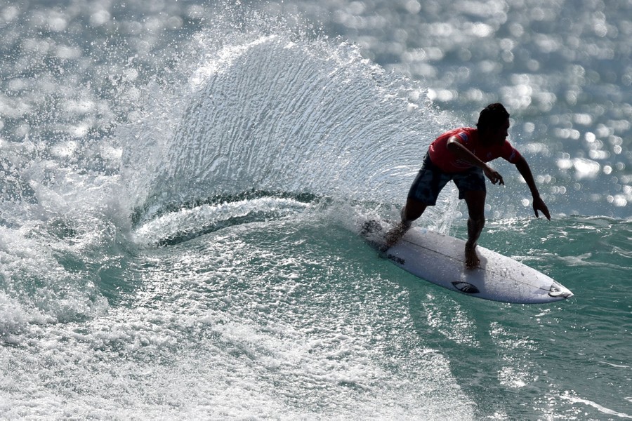 A person surfs on a wave, splashing water behind them.
