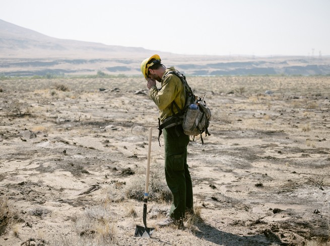 A firefighter rests in the middle of dry and burnt plain.