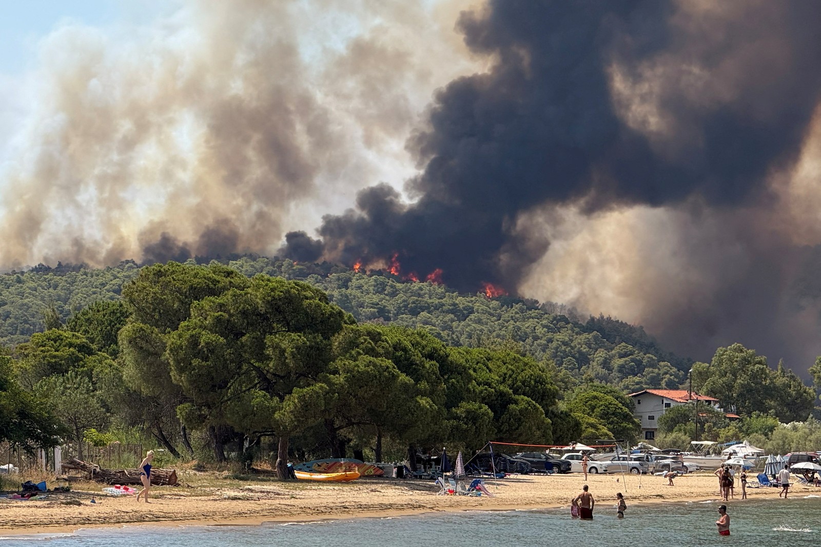 Beachgoers look at rising flames and smoke from a wildfire.