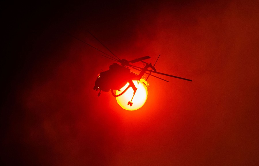 A firefighting helicopter flies in front of the sun.