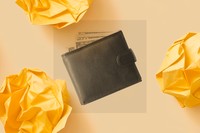 A black and white photo shows a leather wallet with a series of dollar bills coming out of the top