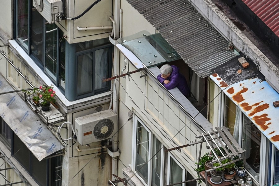 A person stands on a balcony, overlooking a city street.