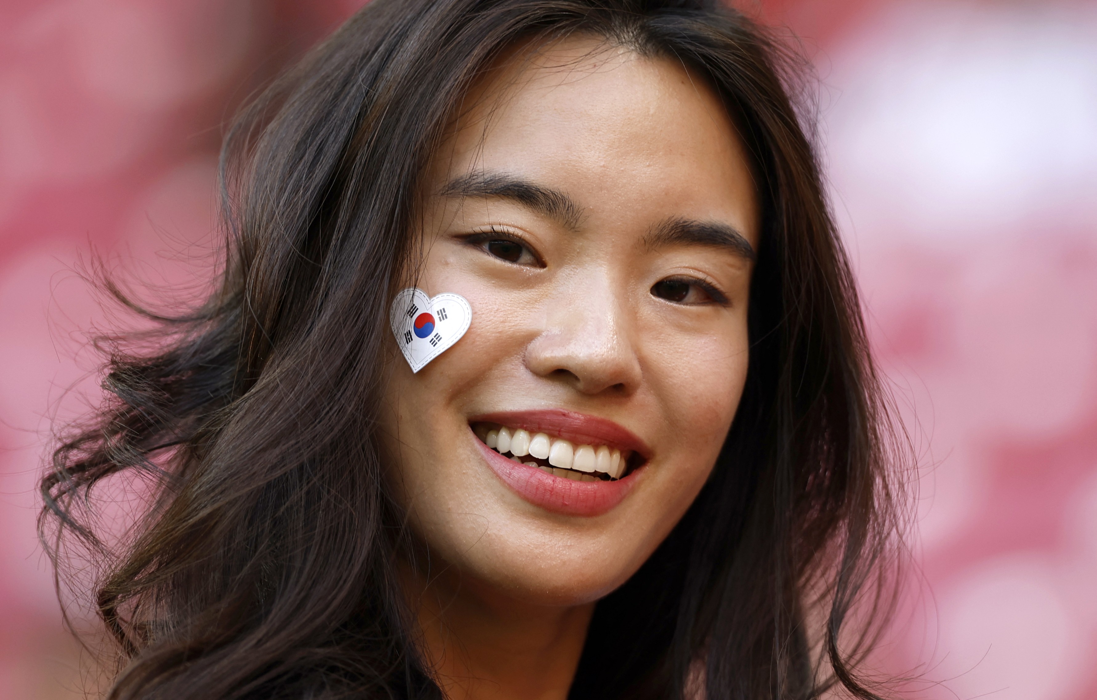 A soccer fan wears a heart-shaped South Korean flag sticker on their cheek.