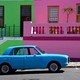 A bright blue car parked in front of pastel pink and green buildings
