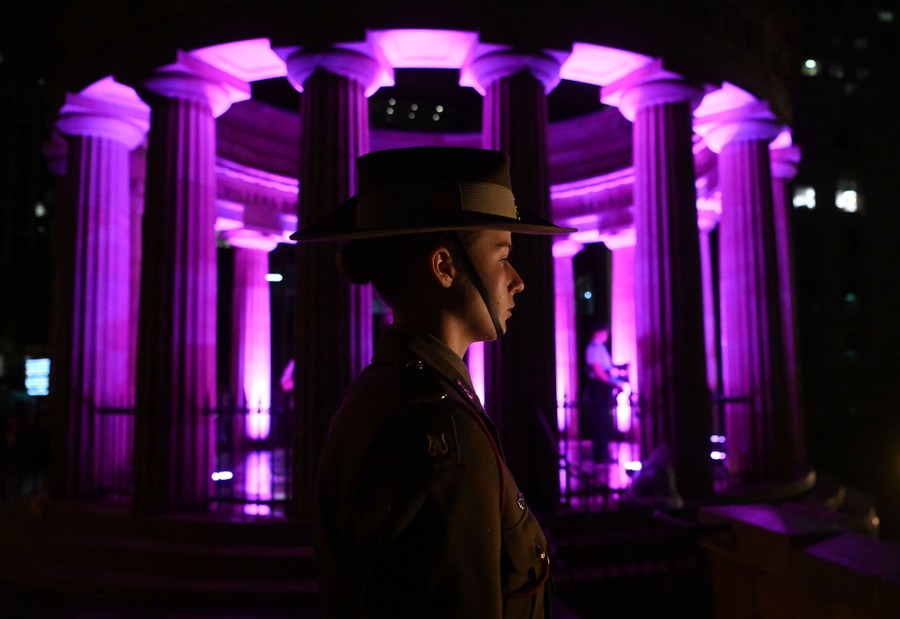 A soldier stands at attention outside a memorial structure at night.