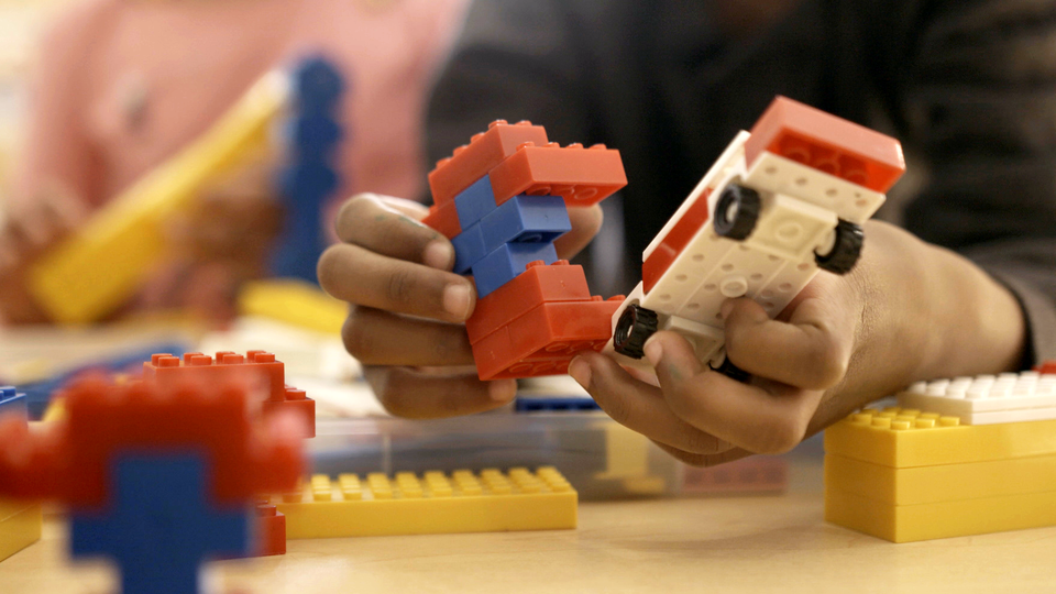 A pair of hands plays with figures made out of Legos.