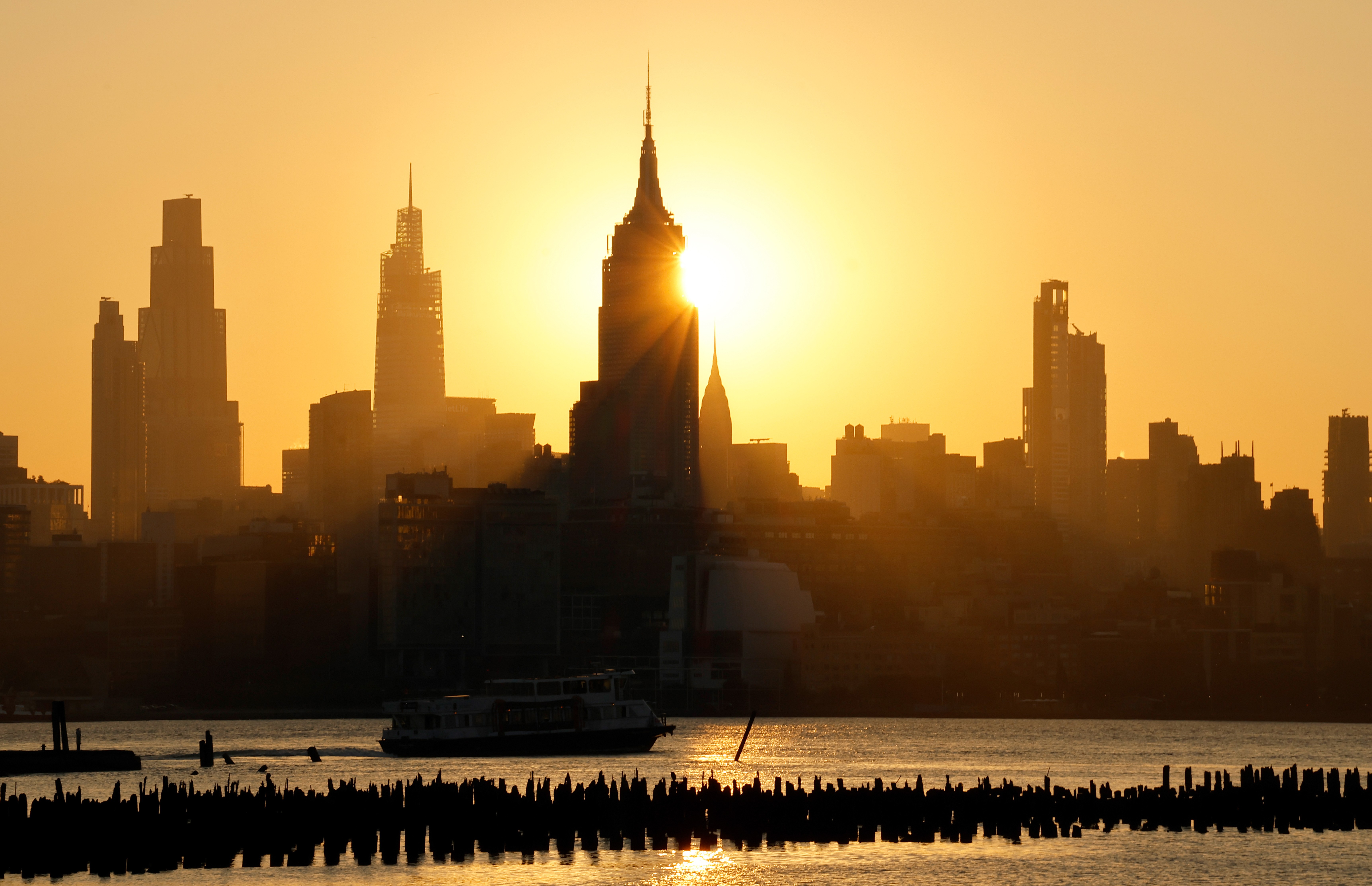 The sun rises behind the skyline of midtown Manhattan on a smoky day.