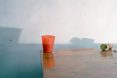 A photo of a red-orange cup on a wooden table, with shadows behind