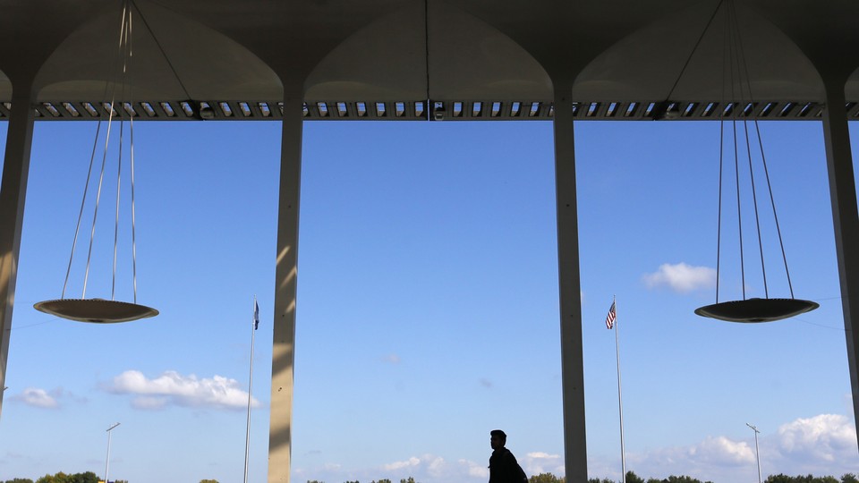 An image of the interior of a building where the silhouette of a person crosses midway through the frame; clear blue skies in the background; four columns visible in the image.