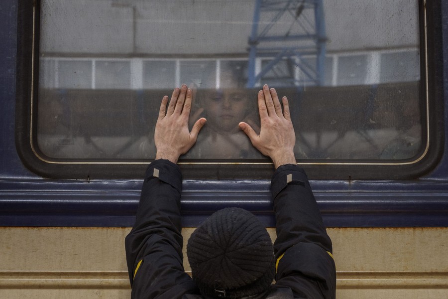 A child looks through a train window at her father outside, who holds both hands up to the window.
