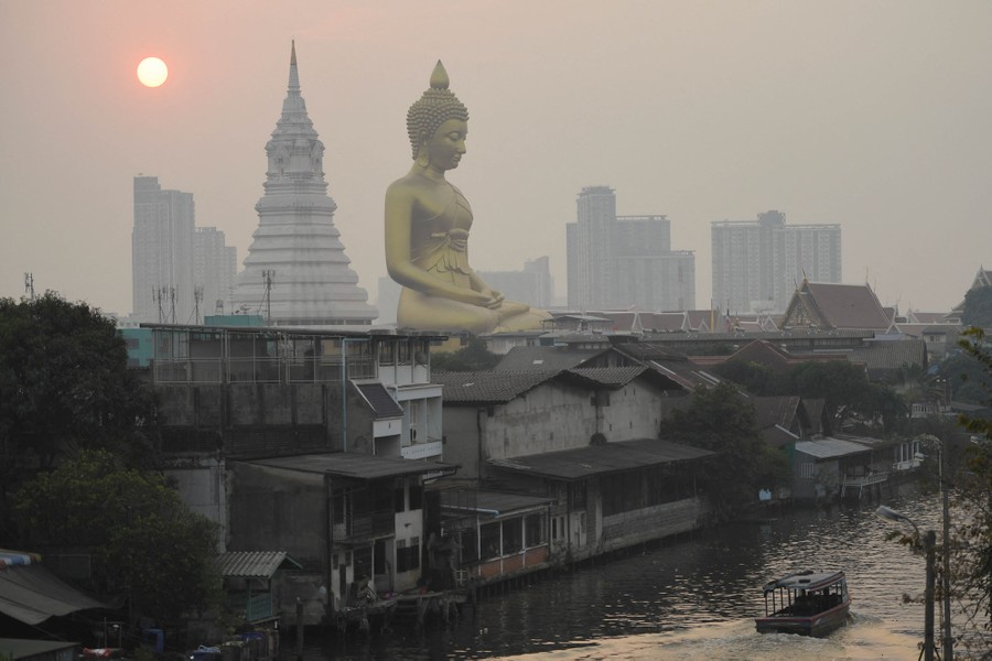 A giant golden Buddha statue sits among smaller buildings under a polluted sky.