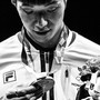 A black and white photo of a man in a track jacket holding a bouquet of flowers and looking down at an Olympic medal while sweat runs down his face