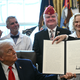 Trump holds up a signed bill in the Oval Office surrounded by smiling onlookers