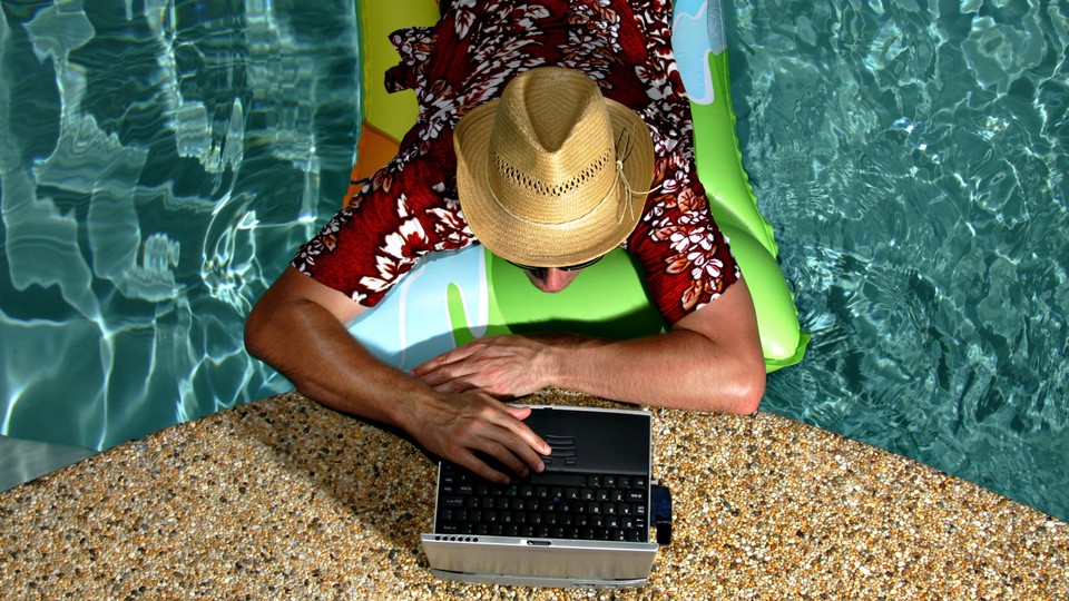 A photo of a man in a pool working on a laptop at the edge of the water.