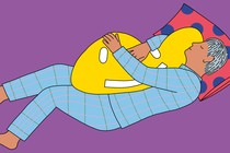 A person sleeping while hugging a pillow shaped like a smiley face