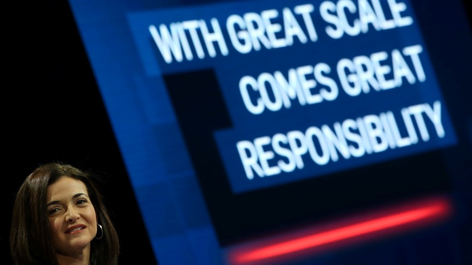 Sheryl Sandberg grimaces in front of a large slide that says “WITH GREAT SCALE COMES GREAT RESPONSIBILITY.”