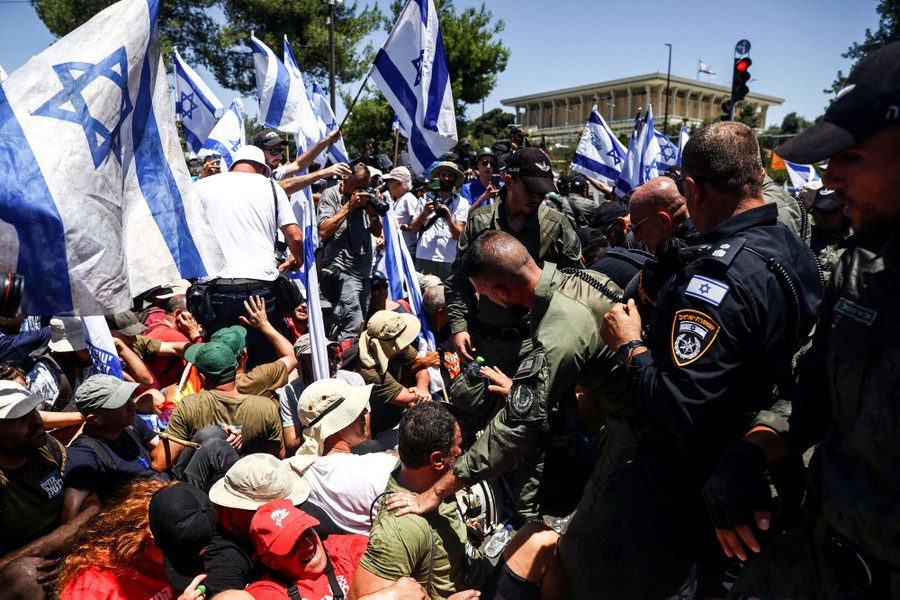 Protesters sit in a street in front of security officers and riot police.